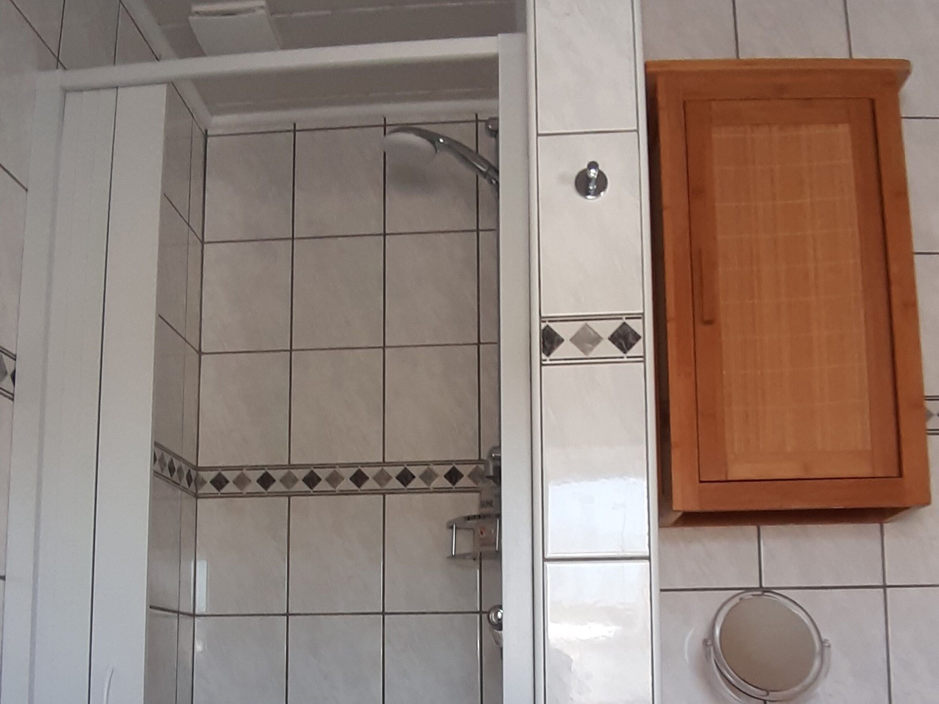 Ein Badezimmer mit Dusche, Holzschrank und gefliesten Wänden.