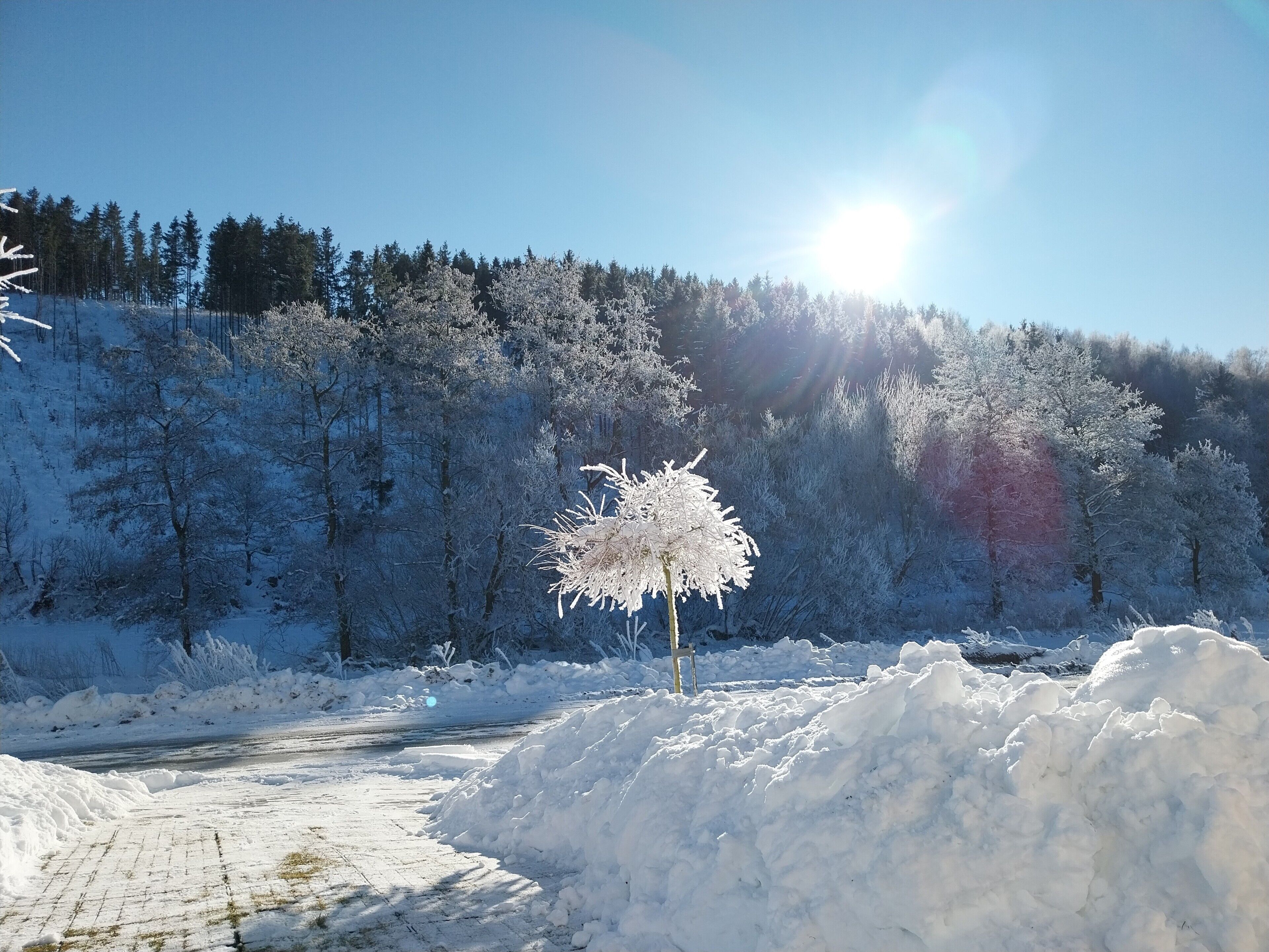A snow-covered landscape with a clear sky, a path, and a pile of snow.
