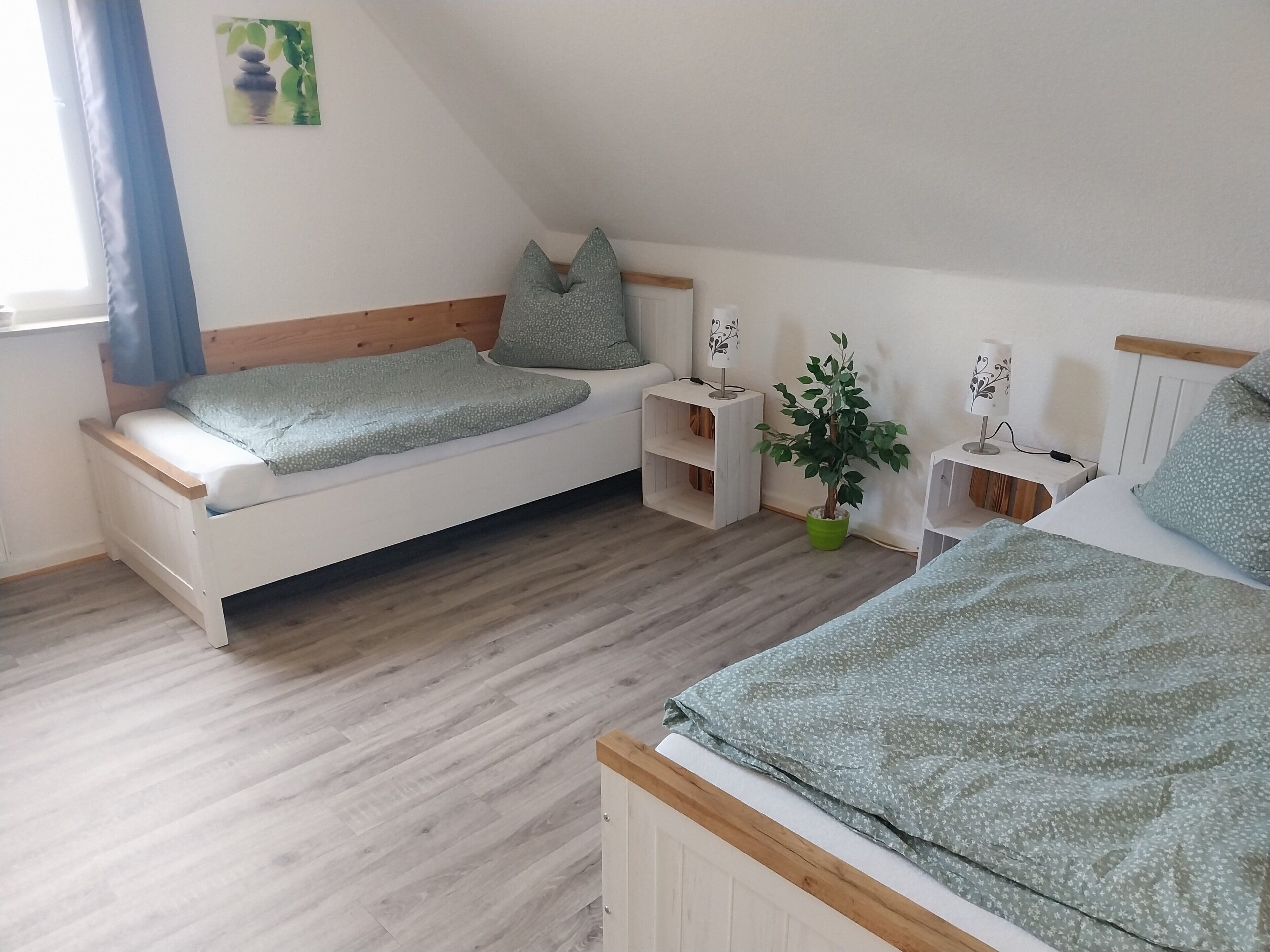 A bedroom with a bed, bedside tables, a nightstand, a potted plant, and a wall-mounted lamp.