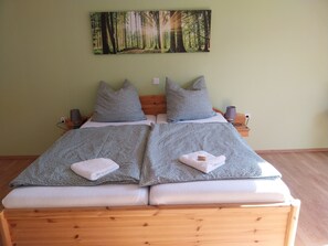 A double bed with grey floral bedding and matching pillows, a wooden headboard, and a forest-themed wall hanging. - Holiday Apartment 'Ferienwohnung Ruhrort' with Private Terrace, Garden and Wi-Fi (Brilon)