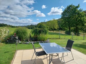 An outdoor patio with a table and chairs, surrounded by a stone wall and greenery. - Holiday Apartment Ruhrort, 70 sqm with Private Terrace, Garden and Wi-Fi (Brilon)