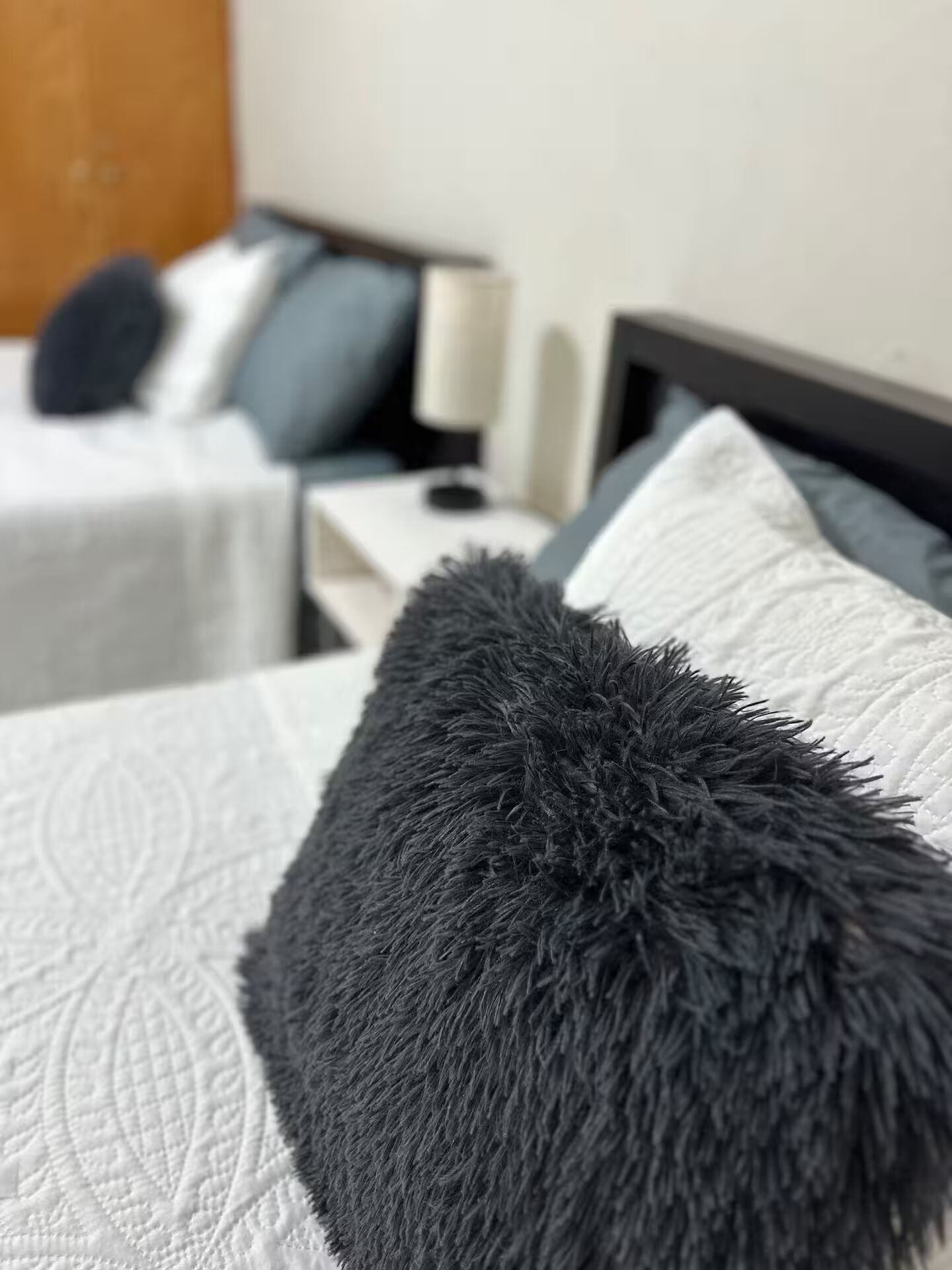 A bed with a dark gray, fluffy pillow and a white quilted bedspread.