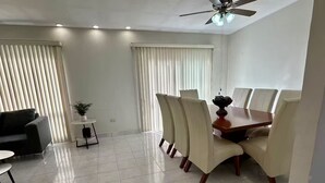 A modern dining area with a wooden table and six chairs, a black sofa, a small round table with a plant, and a ceiling fan.