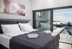 Een moderne slaapkamer met een groot bed, een glazen deur die leidt naar een balkon met een zwembad en een prachtig uitzicht.
