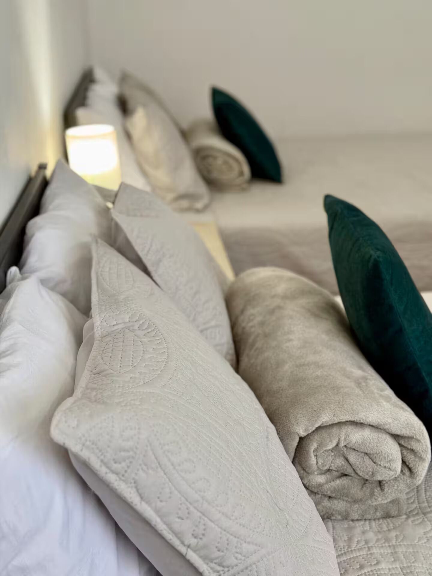 Una cama bien hecha con mantas blancas y grises enrolladas y almohadas color turquesa.