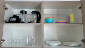 A kitchen with a white tiled backsplash, two shelves with kitchen appliances, and various dishes and glasses.