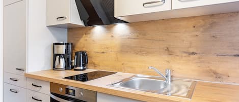 A modern kitchen with white cabinets, a wooden countertop, a built-in oven, and a stainless steel sink.
