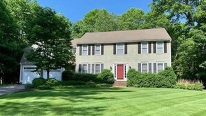 A two-story house with a red door, surrounded by a well-maintained lawn and trees. - Private 4-Bedroom Oasis Near the World Cup Action—Only 9 Miles from Foxboro! (South Easton)