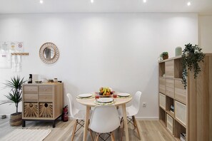 Ein Essbereich mit einem runden Tisch, weißen Stühlen, einem Holzschrank und einem Blumentopf.