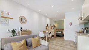 Un salon moderne avec un canapé gris, une table à manger avec des chaises, un coin cuisine et une petite table à manger agrémentée d’une plante.