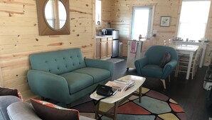 A cozy room with a teal sofa, a grey armchair, and a small coffee table. A kitchen area is visible in the background with a microwave and sink. - Tiny Retreat with boat dock , Lake Hartwell, GA (Martin)