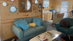 A cozy cabin interior with a sofa, armchair, and a small table with books. - Tiny Retreat with boat dock , Lake Hartwell, GA (Martin)