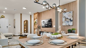 Zona pranzo moderna con tavolo in legno apparecchiato per quattro persone, circondato da sedie imbottite bianche.