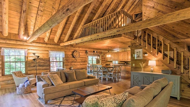 A rustic cabin interior with a wooden ceiling, a dining area, a kitchen, and a staircase.