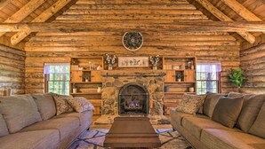 A log cabin interior with a stone fireplace, two sofas, and wooden shelves.