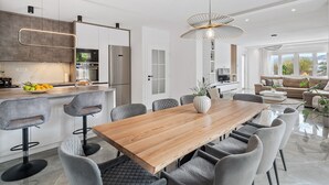 A modern kitchen with a wooden dining table, grey upholstered chairs, and pendant lighting. - Villa Gloria: Stylish 5-Bedroom Retreat with Private Pool and Stunning Valley Views (Zmijavci)