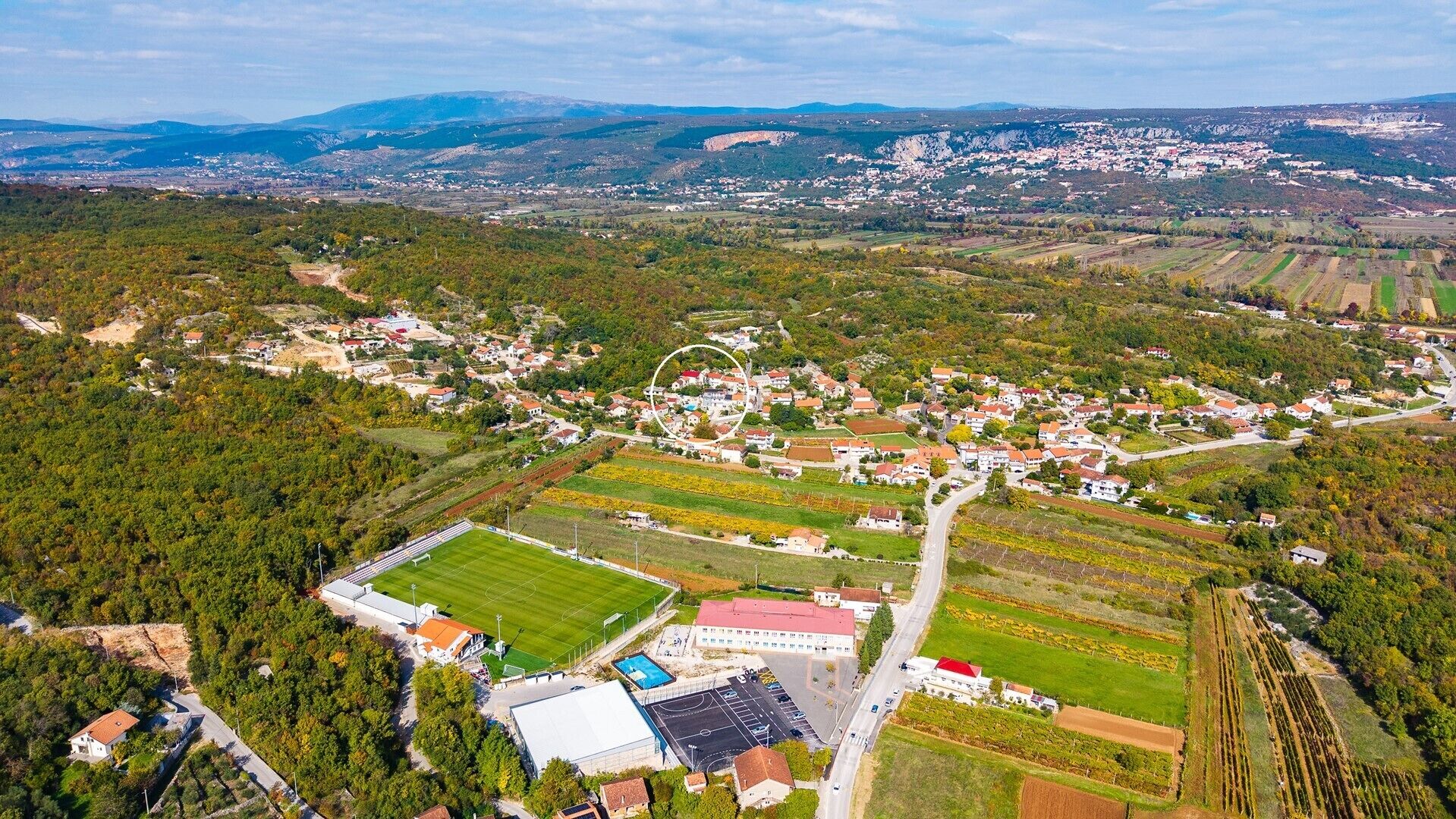 An aerial view of a town with a central road, residential areas, and agricultural fields.