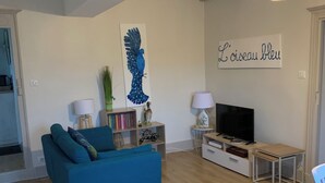 Un saló modern amb un sofà blau, una televisió i una obra d'art penjada a la paret.