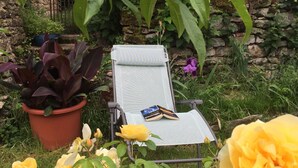 Un jardí amb una cadira de relaxació, una planta en test i roses en flor.