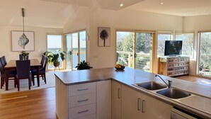 Een moderne keuken met een centraal eiland, een eethoek met tafel en stoelen, en een televisie op een houten kast.