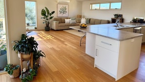 Een moderne keuken met een centraal eiland, een zithoek met een bank en een groot raam dat zorgt voor veel daglicht.