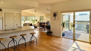 Een ruime keuken met een centraal eiland, houten barstoelen en een eethoek met een tafel en stoelen.