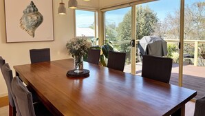 Een eetruimte met een houten tafel, stoelen, hanglampen, een vaas met bloemen en een kunstwerk in een lijst.