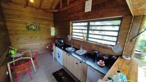 Une cuisine de taille réduite avec des murs en bois, un évier, un lave-linge et une fenêtre avec des stores.
