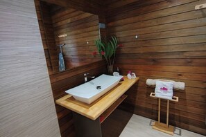 Een houten badkamer met een witte wastafel, een handdoekhouder en een potplant.