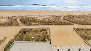 A beach with a fenced area, a pathway, and a building with a flat roof and railings.