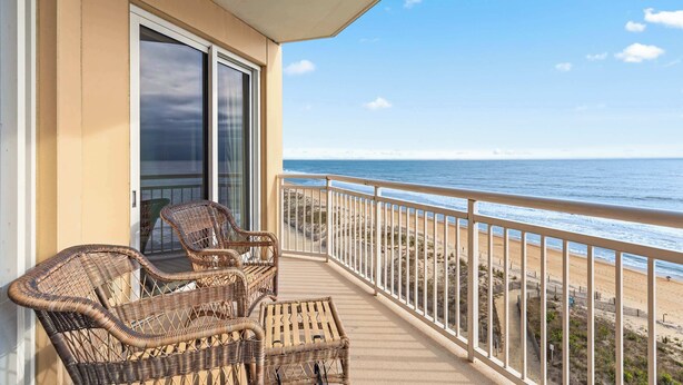 A balcony with wicker furniture overlooking a beach.
