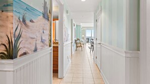 A hallway with a beach mural, white wainscoting, and a view into a dining area.