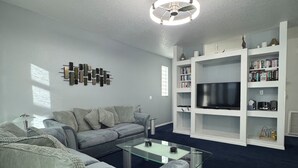 Ett modernt vardagsrum med en grå soffa, ett soffbord i glas och en vit möbel för tv och andra mediaenheter, med böcker och dekorativa föremål.