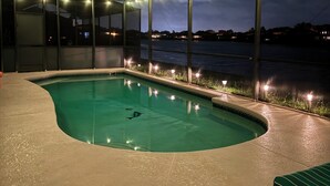 En swimmingpool med en glasvägg runt om, omgiven av ett trädäck och utomhusbelysning.