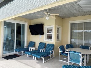Un espacio de estar al aire libre cubierto con sillones reclinables y una mesa, un ventilador de techo y una puerta corrediza de vidrio que da a una piscina.