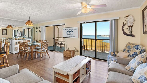 A spacious living area with a dining table, chairs, and a sofa. There is a large window with a view of the beach. - Bay Princess 414 (Ocean City)