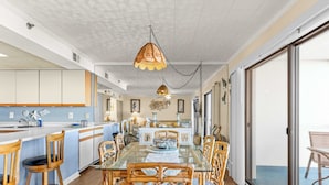 A modern kitchen with white cabinets, a glass dining table, and wicker chairs. - Bay Princess 414 (Ocean City)