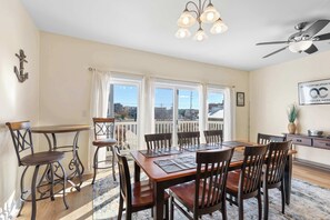 Un comedor con mesa y sillas de madera, una araña y vistas amplias a través de grandes ventanales.