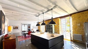 A modern kitchen with a central island, pendant lighting, and a stone wall. - LE MANOIR DES HAUTS DE PIERREVAL: an exceptional stay in the heart of Périgord Noir (Coux et Bigaroque-Mouzens)