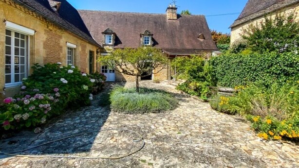 A courtyard with stone paving, a traditional building with a tiled roof, and surrounding greenery. - LE MANOIR DES HAUTS DE PIERREVAL: an exceptional stay in the heart of Périgord Noir (Coux et Bigaroque-Mouzens)