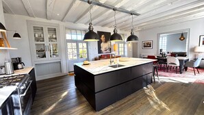A modern kitchen with a central island, pendant lighting, and a dining area with a red sofa and chairs. - LE MANOIR DES HAUTS DE PIERREVAL: an exceptional stay in the heart of Périgord Noir (Coux et Bigaroque-Mouzens)