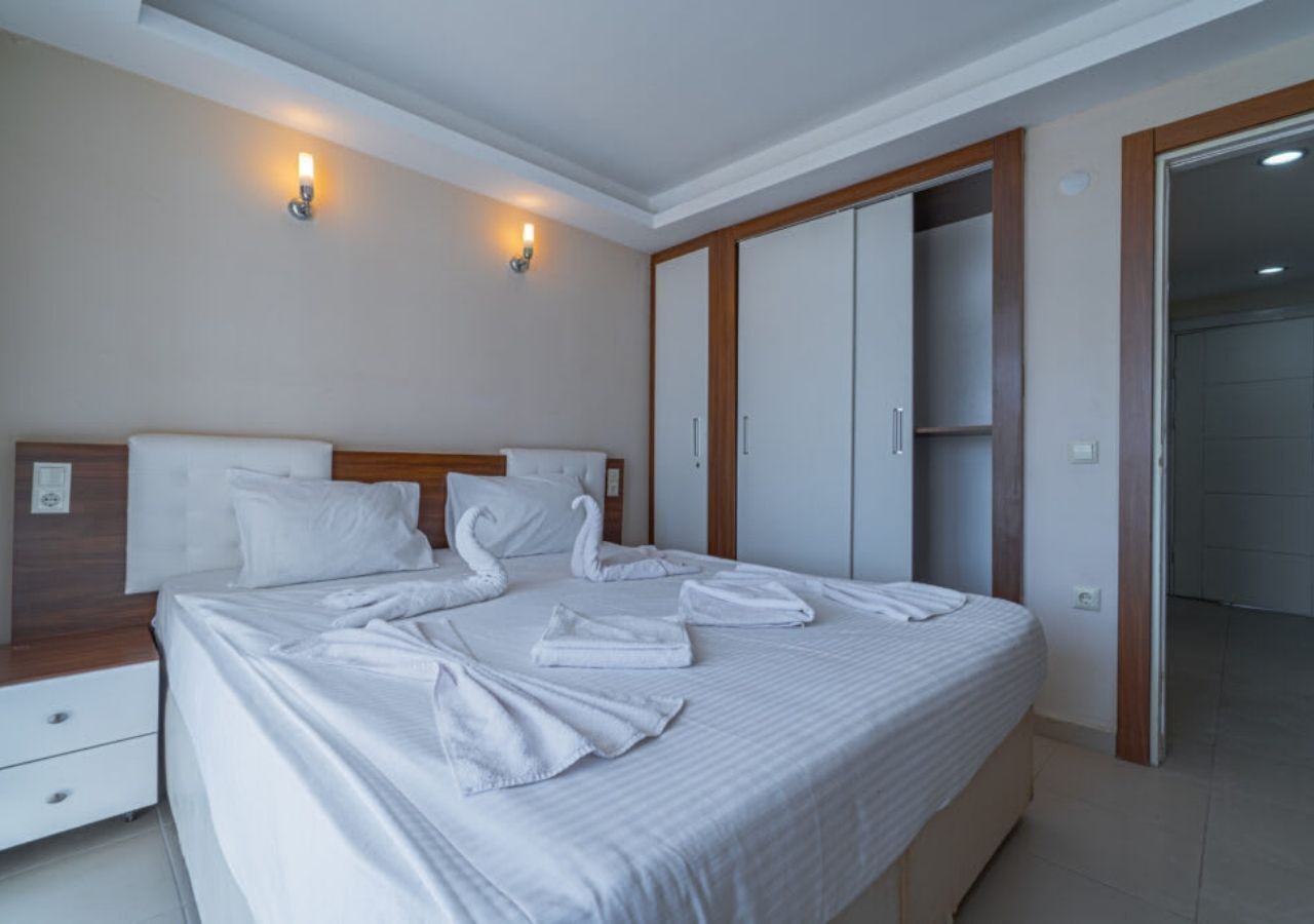 A neatly made bed with towels arranged in a swan shape, a wooden headboard, a nightstand, and a wardrobe with sliding doors.