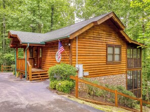 A log cabin with a porch, an American flag, and a stone foundation.