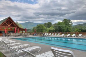 A pool area with lounge chairs and a wooden building with a sloped roof. - Quilted Pines – Hot Tub, Pool, Dog Friendly (Sevierville)