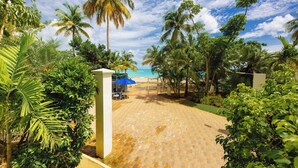 A paved pathway leading to a beach area with palm trees and a blue umbrella. - OASIS 2BR/2Bath STEPS from BEACH + Parking @ ESJ (Carolina)