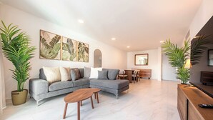 A modern living room with a grey sectional sofa, a wooden coffee table, and two potted plants. - OASIS 2BR/2Bath STEPS from BEACH + Parking @ ESJ (Carolina)