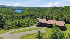 A lodge with a red roof, surrounded by lush greenery and a lake. - Hiwassee Lake Lodge - Private Mtn-Top Retreat - Lake Views - Sleeps 13 (Murphy)
