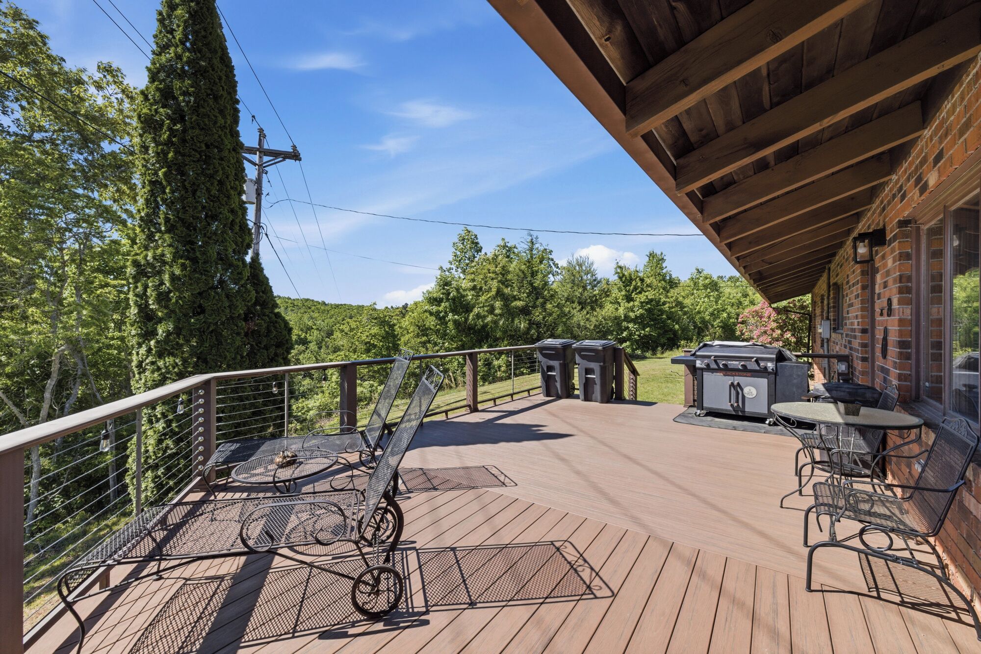 A covered deck with outdoor seating, a grill, and a view of the surrounding forest.