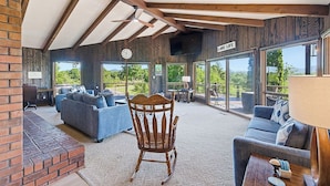 A spacious living area with a wooden rocking chair, sofas, and large windows offering a view of greenery. - Hiwassee Lake Lodge - Private Mtn-Top Retreat - Lake Views - Sleeps 13 (Murphy)