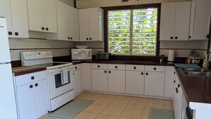 A kitchen with white cabinets, a stove, a microwave, and a window with a view of greenery. - Ocean Nest - 4-bedroom beach-front house in La Playa, Anasco Puerto Rico (La Playa)